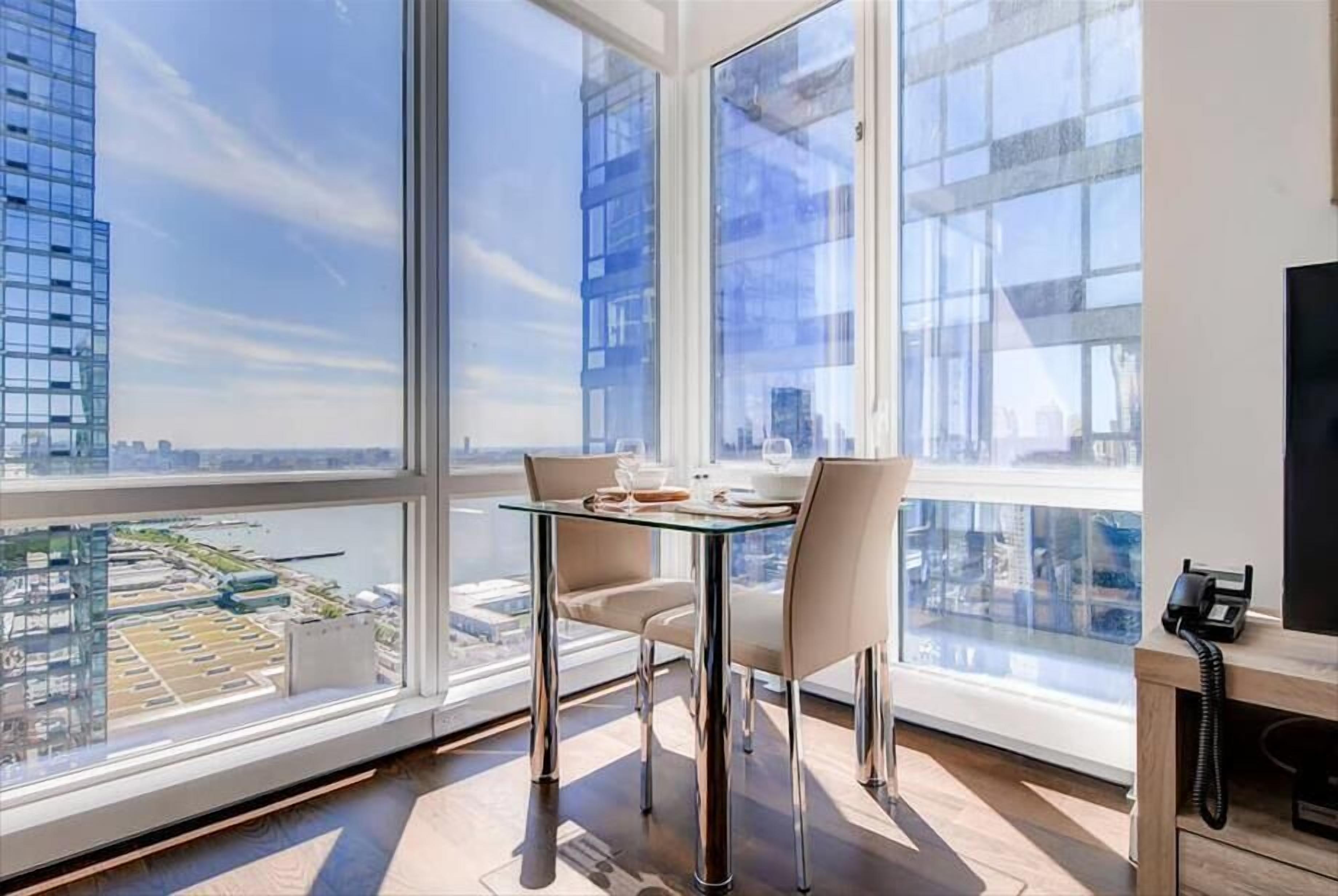 A modern office space with a large window, a glass table, two chairs, and a desk with a telephone.