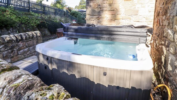 Un jacuzzi en un entorno rústico al aire libre, con paredes de piedra y una valla de madera.