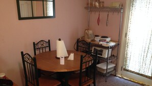 A dining area with a round table, four chairs, a wall-mounted mirror, and a shelf with kitchen items. - Cabin in Bankhead National Forest (Moulton)