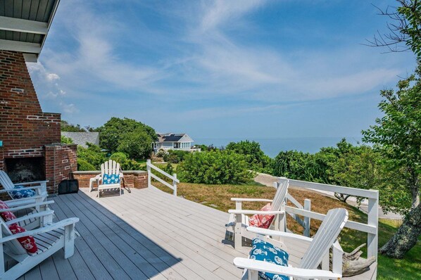 Um deck com cadeiras Adirondack, uma lareira de tijolos e vista para o oceano.