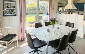 A dining area with a round table, chairs, a vase with flowers, and a window with curtains.