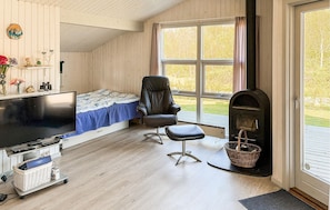 A cozy room with a bed, a chair, a fireplace, a TV, and a window with a view of greenery.