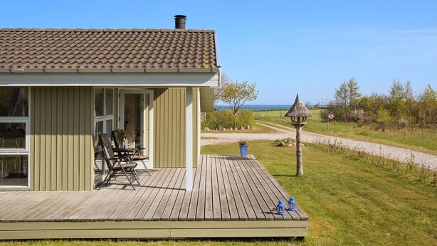 Ett hus med en träveranda, en matplats med stolar och ett bord samt utsikt över havet.