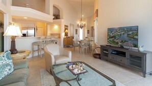 A spacious living room with a dining area, kitchen, and a large TV on the wall.