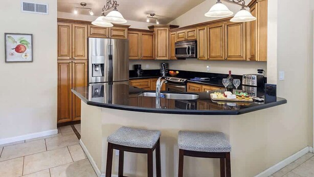 Una cocina con gabinetes de madera, un refrigerador de acero inoxidable, un microondas y una isla grande con taburetes.