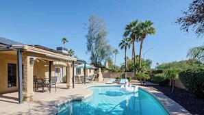 Una piscina con flotadores con forma de cisne, mobiliario de exterior y palmeras.