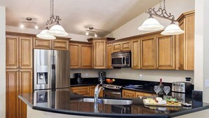 Una cocina moderna con armarios de madera, electrodomésticos de acero inoxidable, una isla grande con lavamanos e iluminación colgante.