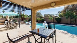 Un espacio al aire libre techado con piscina, sillones de descanso y una mesa.