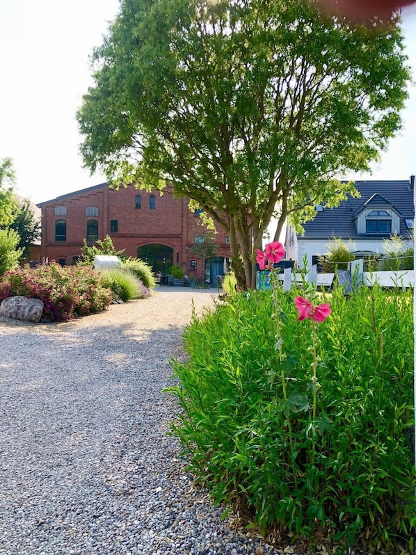 A gravel path leading to a brick building with a large tree in the foreground.