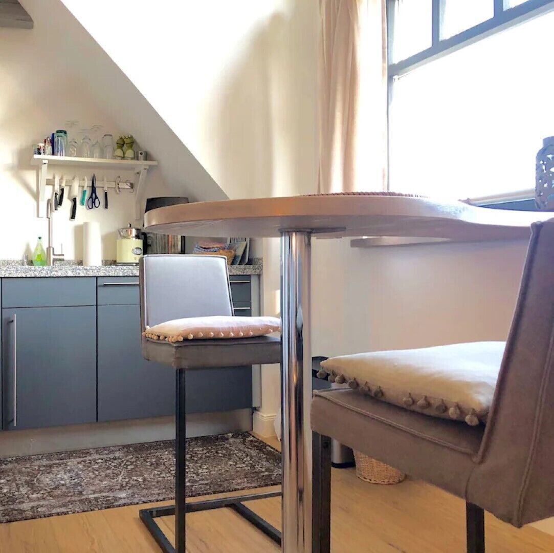 Une cuisine compacte avec un coin repas, comprenant une petite table et deux chaises, un îlot de cuisine et une fenêtre avec des rideaux.