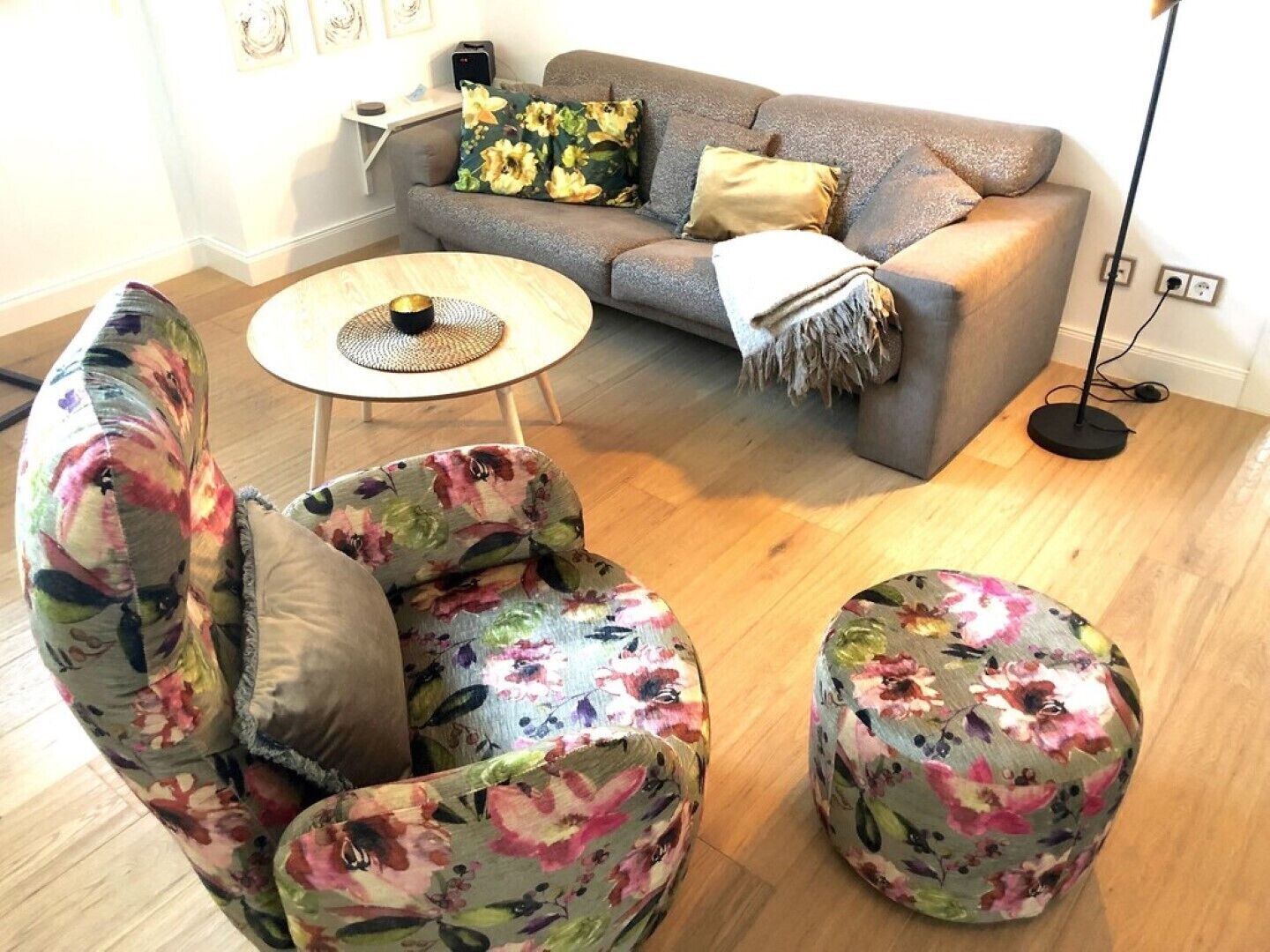 A living room with a grey sofa, floral armchair, ottoman, and a round coffee table.