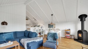 A modern living room with a blue sofa, a fluffy chair, a wooden coffee table, and a black wood stove.