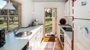 Cocina compacta con lavabo, estufa y armarios, que da a una puerta que se abre a un jardín.
