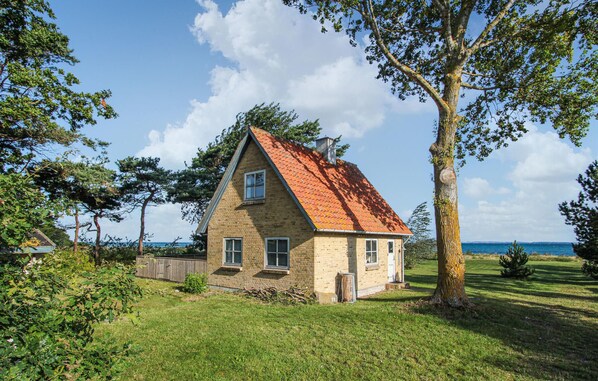 Une maison de plain-pied avec un toit recouvert de tuiles rouges, entourée d’une pelouse bien entretenue et d’arbres.