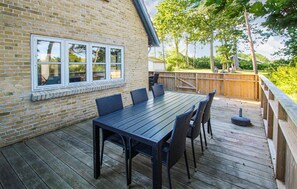 Une terrasse avec une table et des chaises en bois, un mur en briques et une fenêtre.
