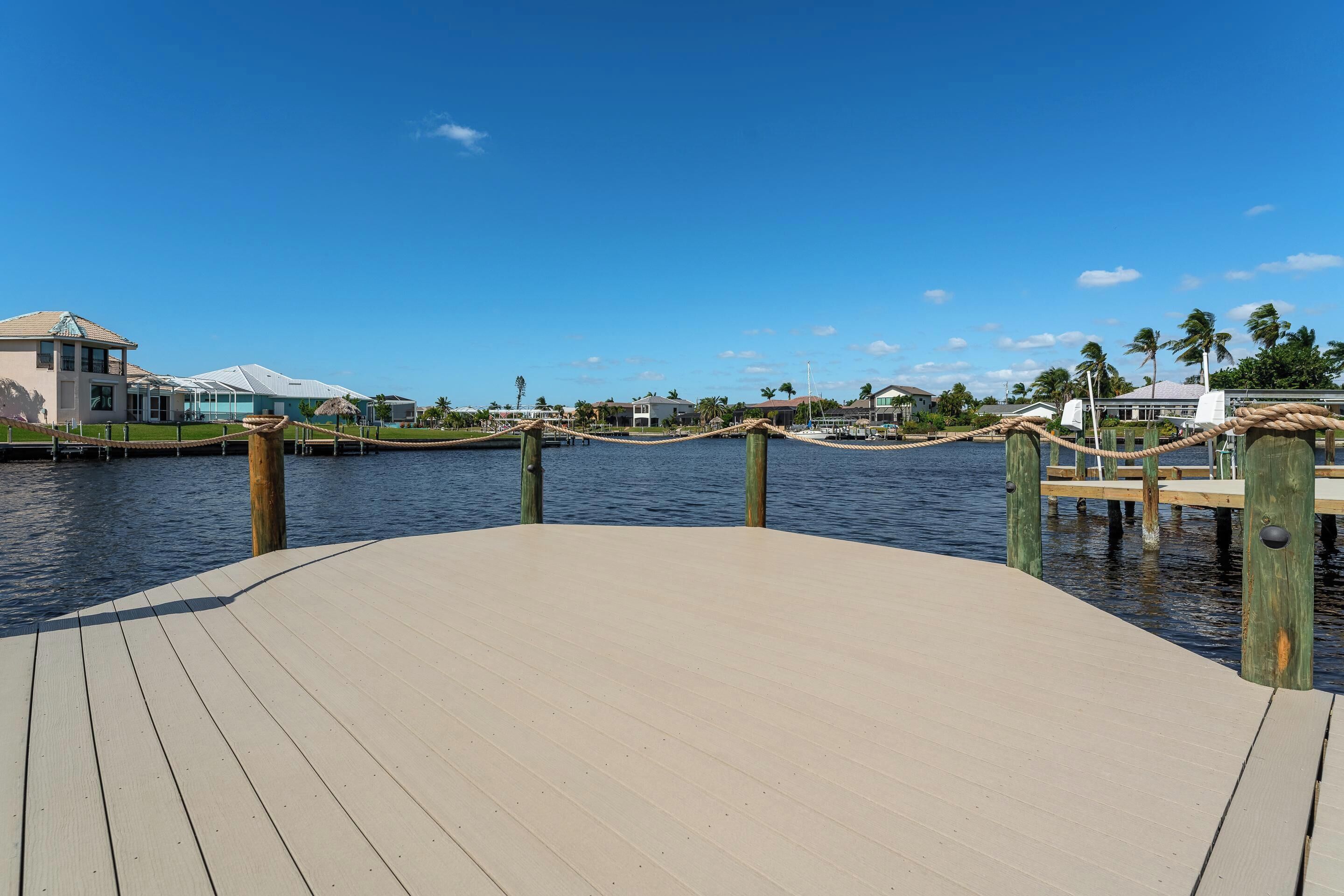 Eine Uferpromenade mit Holzsteg, Seilgeländer und freiem Blick auf das Wasser sowie entfernte Gebäude.