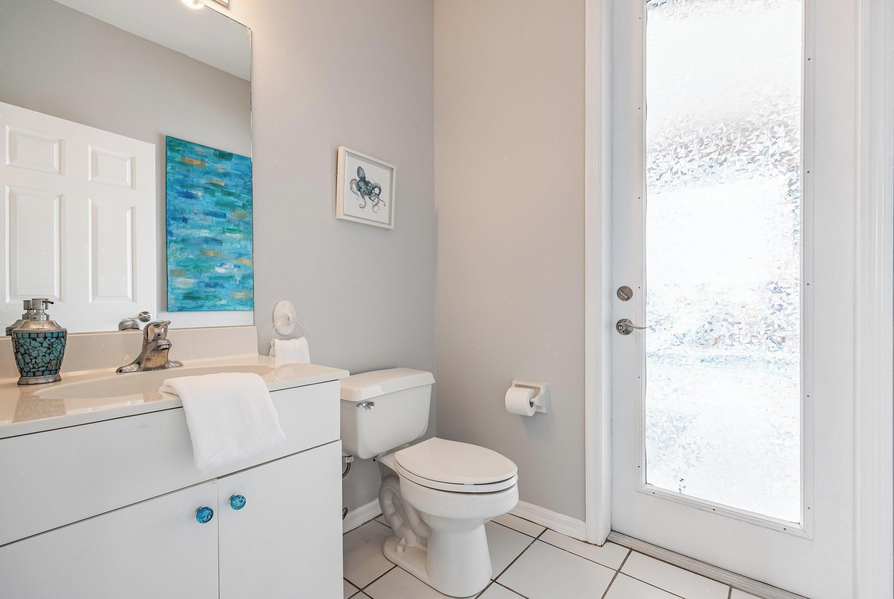Un baño con un inodoro blanco, un lavabo con un florero azul y un cuadro en la pared.