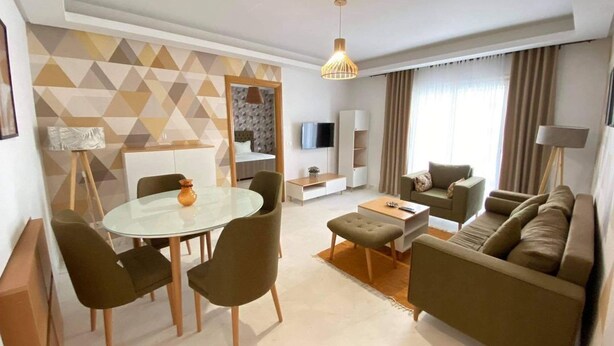 A modern living room with a round dining table, green sofas, a TV, and a geometric-patterned wall. - Apparently new ideal for family (Avignon)