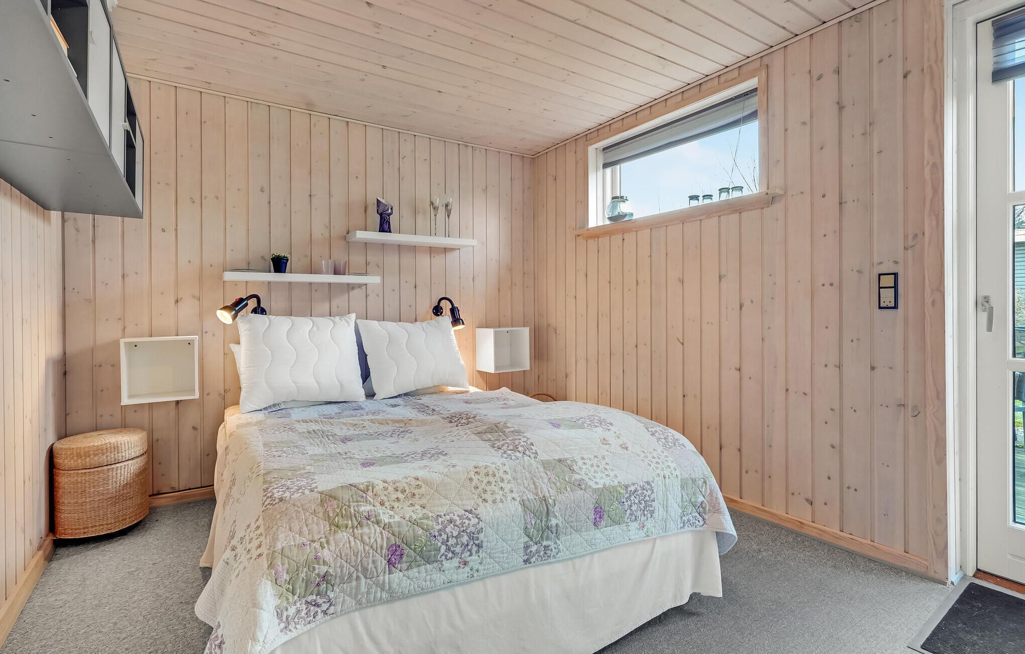 A bedroom with a bed, bedside lamps, a window, and wooden walls.