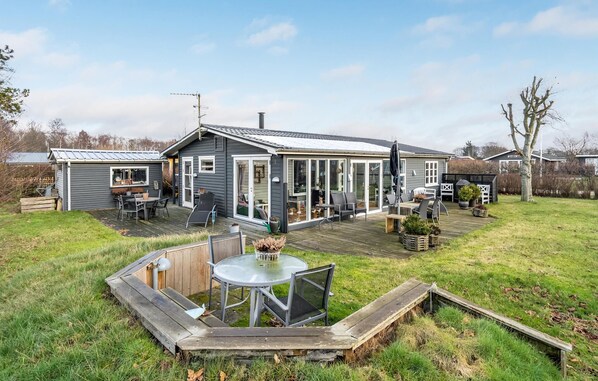 A house with a patio area featuring a round table and chairs, a small deck, and a garden with potted plants. - Cozy home in Hadsund with WiFi (Hadsund)