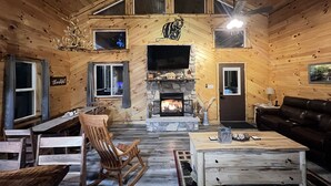 A cozy cabin interior with a stone fireplace, wooden walls, a television mounted above it, and a leather sofa. - Secluded 3 bedroom Log Cabin,Kid Friendly,In Logan Ohio,in Hocking Hills,Hot Tub (Logan)