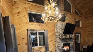 A cozy log cabin interior with a dining area, stone fireplace, and a large window. - Secluded 3 bedroom Log Cabin,Kid Friendly,In Logan Ohio,in Hocking Hills,Hot Tub (Logan)