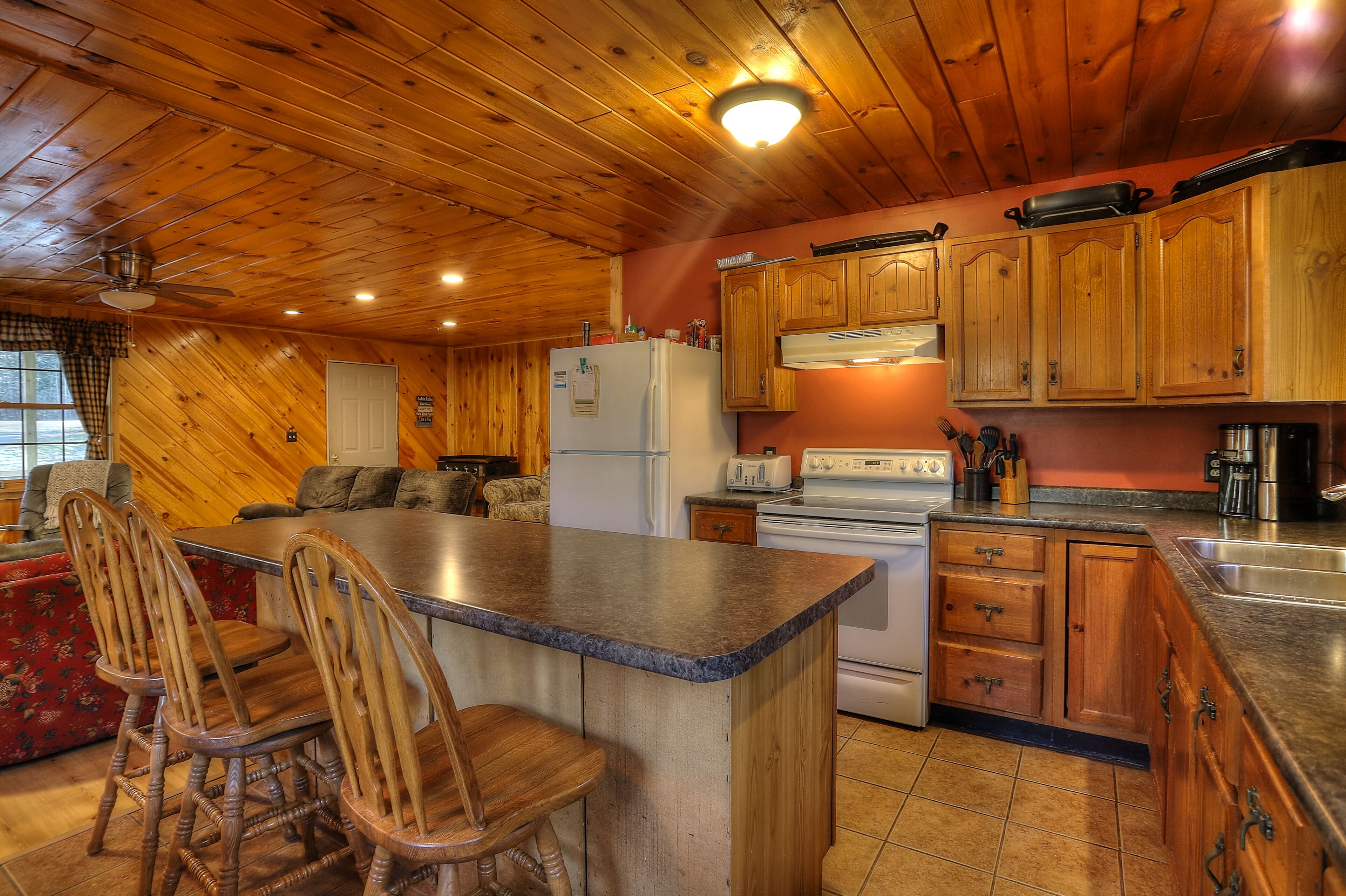 A kitchen with wooden cabinets, a refrigerator, a stove, and a dining area with chairs.