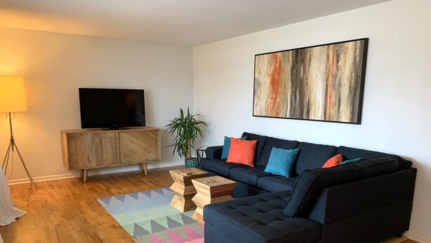 A modern living room with a sectional sofa, a flat-screen TV, a wooden cabinet, and a colorful rug. - Welcome to Holiday House! Cozy, modern home 7 min. from the beach and wineries. (Stevensville)