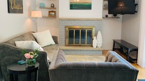 A living room with a fireplace, a ceiling fan, a TV mounted on the wall, and a sofa. - Welcome to Holiday House! Cozy, modern home 7 min. from the beach and wineries. (Stevensville)