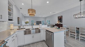 Une cuisine moderne avec des meubles blancs, un îlot central, des appareils en acier inoxydable et un luminaire suspendu.