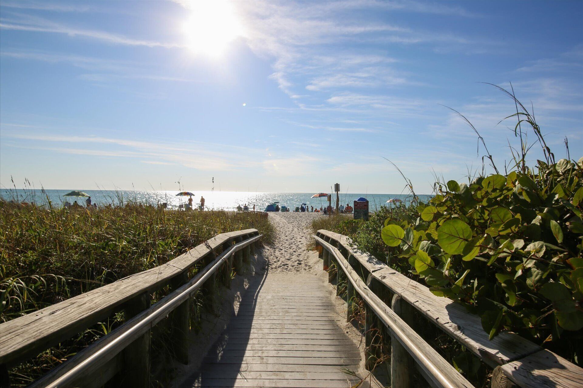 A wooden boardwalk leading to a beach with people and umbrellas.