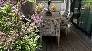 Eine Terrasse im Freien mit Tisch, Stühlen, einem großen Sonnenschirm und Blumentöpfen.
