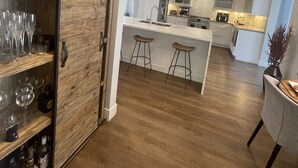 Eine moderne Küche mit Holzschränken, einer zentralen Kochinsel mit Hockern und einem Weineckfach mit Gläsern.