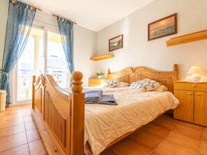 Een slaapkamer met een houten bed, een nachtkastje met een lamp, een raam met gordijnen en een foto aan de muur.