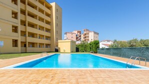 A swimming pool with tiled flooring, surrounded by a building with multiple balconies and a clear blue sky. - Beautiful apartment for 4 people with WIFI, pool, TV and terrace (Roses)