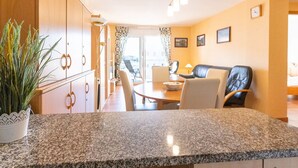 A modern kitchen with granite countertops, a dining area with a table and chairs, and a living area with a sofa and a TV. - Beautiful apartment for 4 people with WIFI, pool, TV and terrace (Roses)
