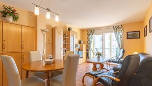A cozy living room with a dining area, wooden cabinets, a sofa, and a balcony with curtains. - Beautiful apartment for 4 people with WIFI, pool, TV and terrace (Roses)