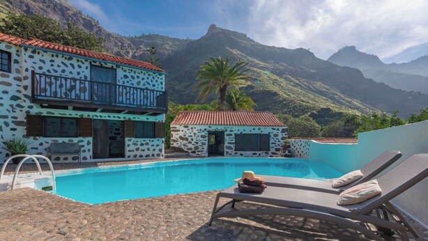 Zona junto a la piscina con un edificio de diseño de piedra, una silla de descanso y vistas a montañas.