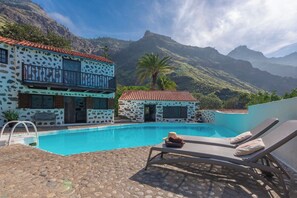 Un espace aménagé au bord de la piscine, avec un b âtiment aux motifs en pierre, un fauteuil de relaxation et une vue sur les montagnes.