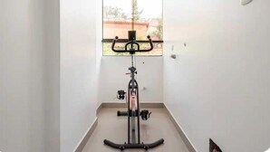 En motionscykel i et rum med et vindue, hvide vægge og et flisegulv.