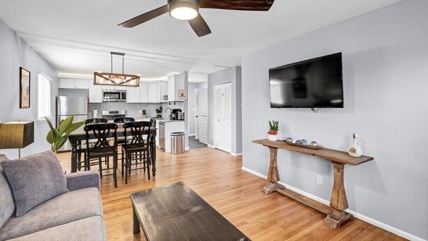 A modern living room with a ceiling fan, a flat-screen TV mounted on the wall, and a dining area with a wooden table and chairs. - Bourbon House 4 - The Wellingmoor - Hot Tub (Louisville)