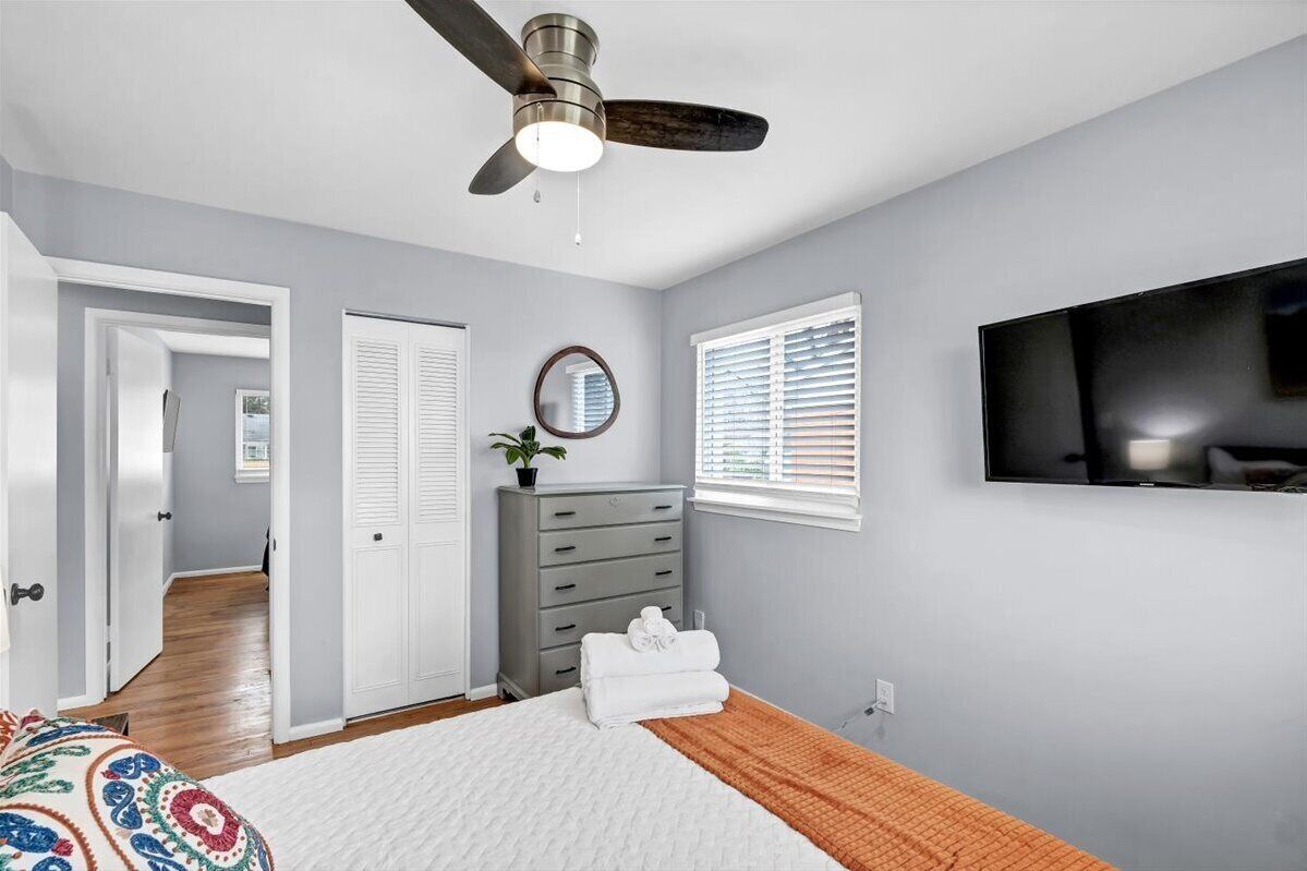 A bedroom with a bed, a dresser, a ceiling fan, a TV, and a window with blinds.