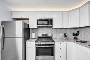 Enjoy cooking in this well-equipped kitchen with a refrigerator, microwave, and oven, along with a herringbone-patterned backsplash and granite countertop.
