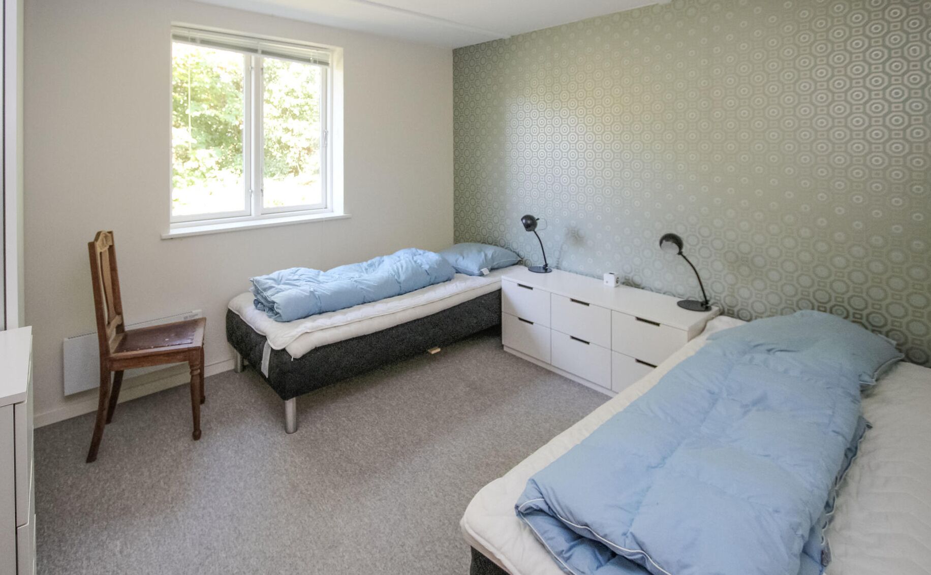 A bedroom with a single bed, a chair, a desk, and a window.