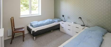 A bedroom with a single bed, a chair, a desk, and a window.