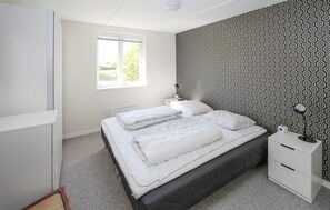Een slaapkamer met een bed, nachtkastje, kledingkast en een raam met jaloezieën.