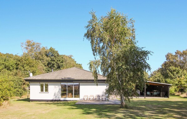 Een gelijkvloers huis met pannendak, een overdekte patio en een grote boom ervoor.