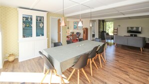 A spacious dining area with a long table, chairs, and pendant lighting. There is a television and a sofa in the adjacent living area. - Awesome home in Samsø with sauna (Samsø)