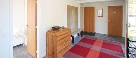Ein Flur mit einer hölzernen Bank, einem Holzschrank und einem rot-grauen Karottenteppich.