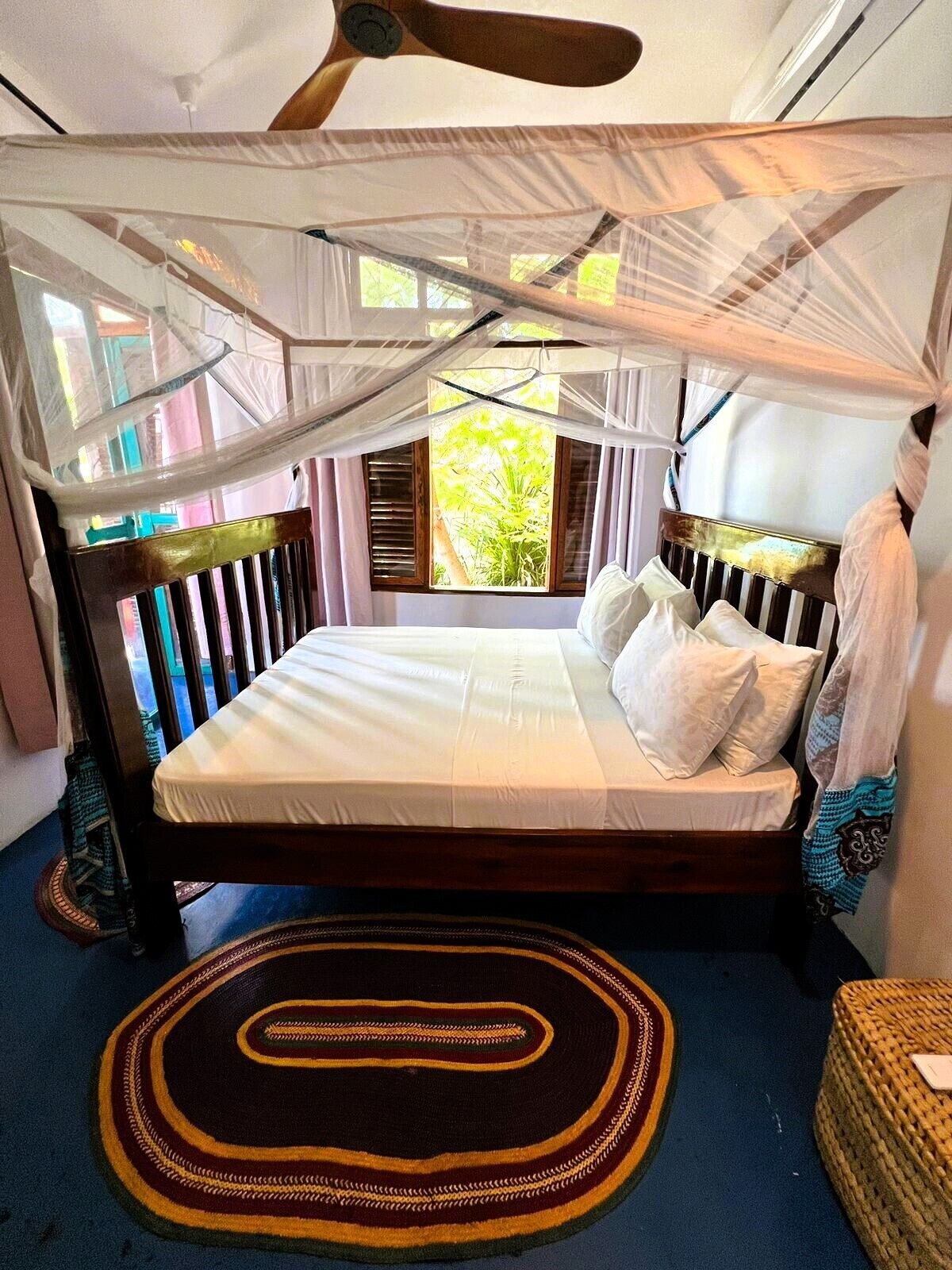 A bed with a canopy, a wooden headboard, and a view of greenery outside.